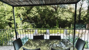 A covered outdoor seating area with a table and chairs, surrounded by a metal fence and lush greenery. - Riverfront house with pool at the foot of the Cascades du Sautadet (La Roque-Sur-Cèze)