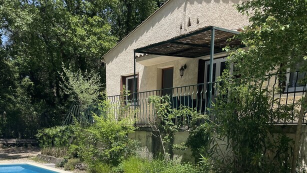 A swimming pool with two lounge chairs, surrounded by greenery and a building with a balcony. - Riverfront house with pool at the foot of the Cascades du Sautadet (La Roque-Sur-Cèze)