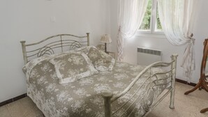 A bed with a metal frame and floral bedding, a bedside lamp, a window with sheer curtains, and a radiator. - Riverfront house with pool at the foot of the Cascades du Sautadet (La Roque-Sur-Cèze)