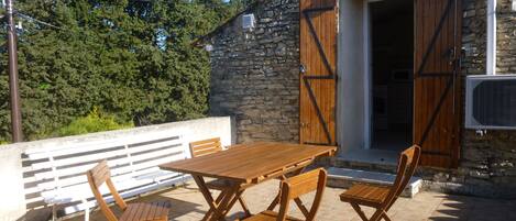 An outdoor patio with a stone wall, wooden furniture, and a stone building with open wooden doors.