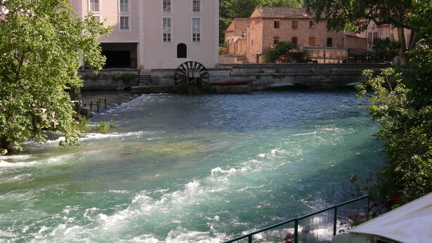 A river with a water wheel, surrounded by buildings and greenery. - furnished studio overlooking the luberon (Lagnes)
