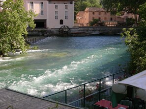 Une rivière avec une roue à eau, entourée de bâtiments et de verdure.