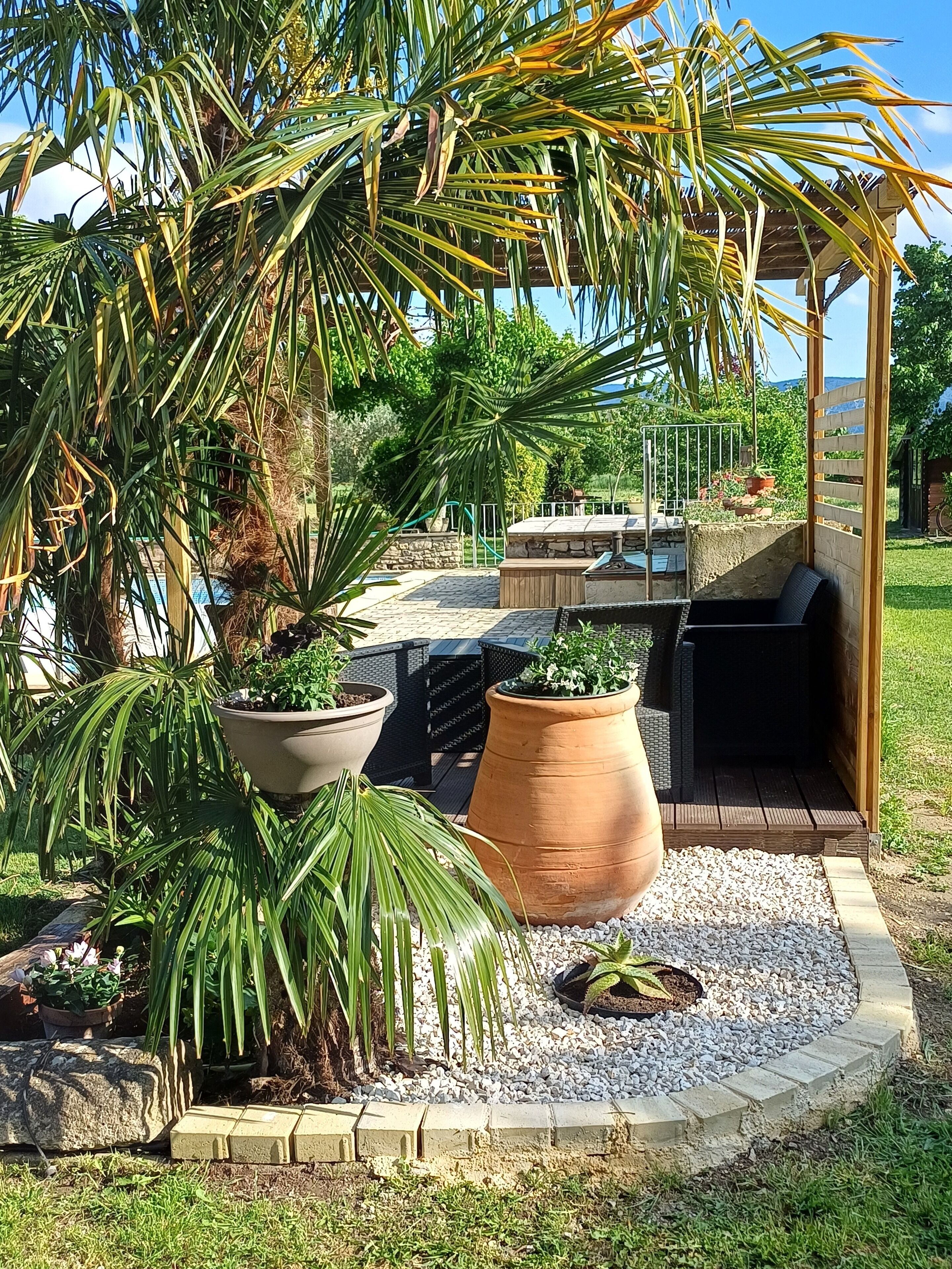 En uteplats med en pergola, krukväxter, en grill och en gång av sten.