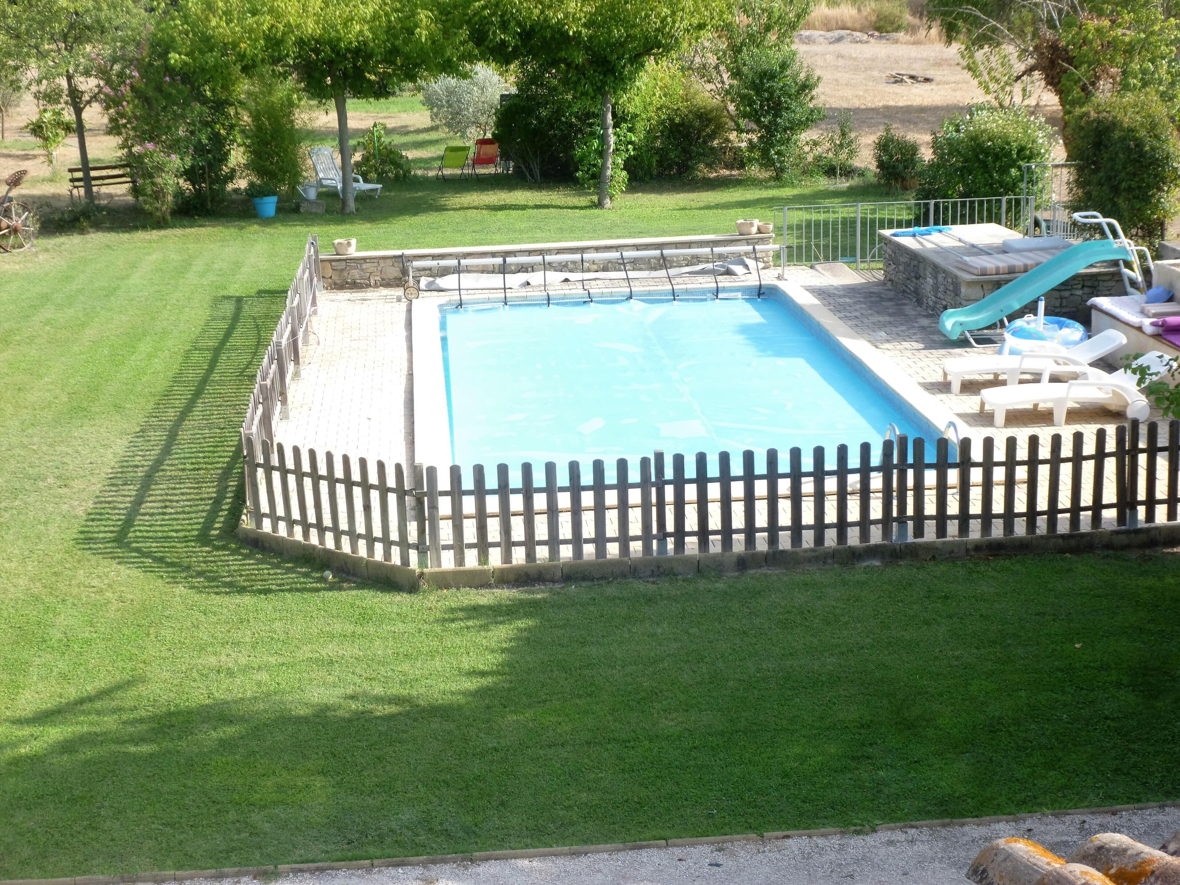 Una piscina rectangular con valla de madera, rodeada de un césped cuidado.