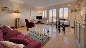 A living room with a sofa, a glass coffee table, a TV, and a dining area with chairs and a table.