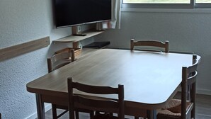 Un comedor con una mesa y sillas, un televisor en la pared y una ventana con vistas a un paisaje verde.