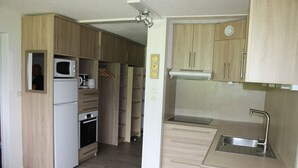 Una cocina compacta con armarios de madera, microondas integrado, cafetera y lavabo.