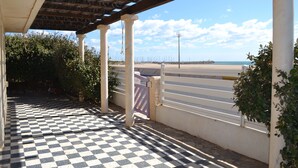 Ein überdachter Außenbereich mit Schachbrettmuster-Boden, Säulen und Blick auf den Strand.