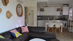 Ein modernes Wohnzimmer mit einer schwarzen Ledersofa, einem runden weißen Couchtisch und einer Küchenzeile mit weißen Schränken und einem Esstisch.