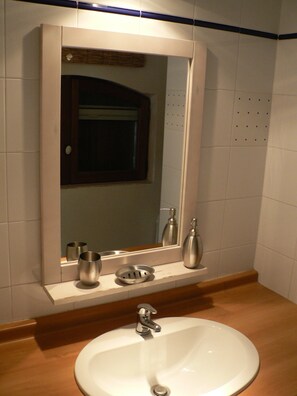 Un baño con un lavamanos blanco, un espejo y una encimera de madera.