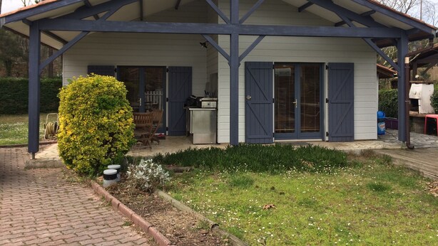 A covered outdoor area with a wooden bench and a small table, surrounded by a garden with a hedge and a bush. - RENTAL HOUSE MESSANGES near beach south coast of Landes  (Messanges)
