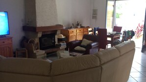 A living room with a large beige sectional sofa, a fireplace, a television, and a dining area with chairs and a table. - RENTAL HOUSE MESSANGES near beach south coast of Landes  (Messanges)
