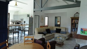 A spacious living area with a sofa, coffee table, and a dining table with chairs. There is a kitchen in the background with cabinets and a refrigerator. - RENTAL HOUSE MESSANGES near beach south coast of Landes  (Messanges)