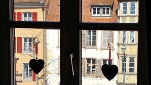 A window with heart-shaped decorations and a view of buildings with red shutters and a tiled roof. - Wonderful apartment in the heart of Little Venice (Colmar)
