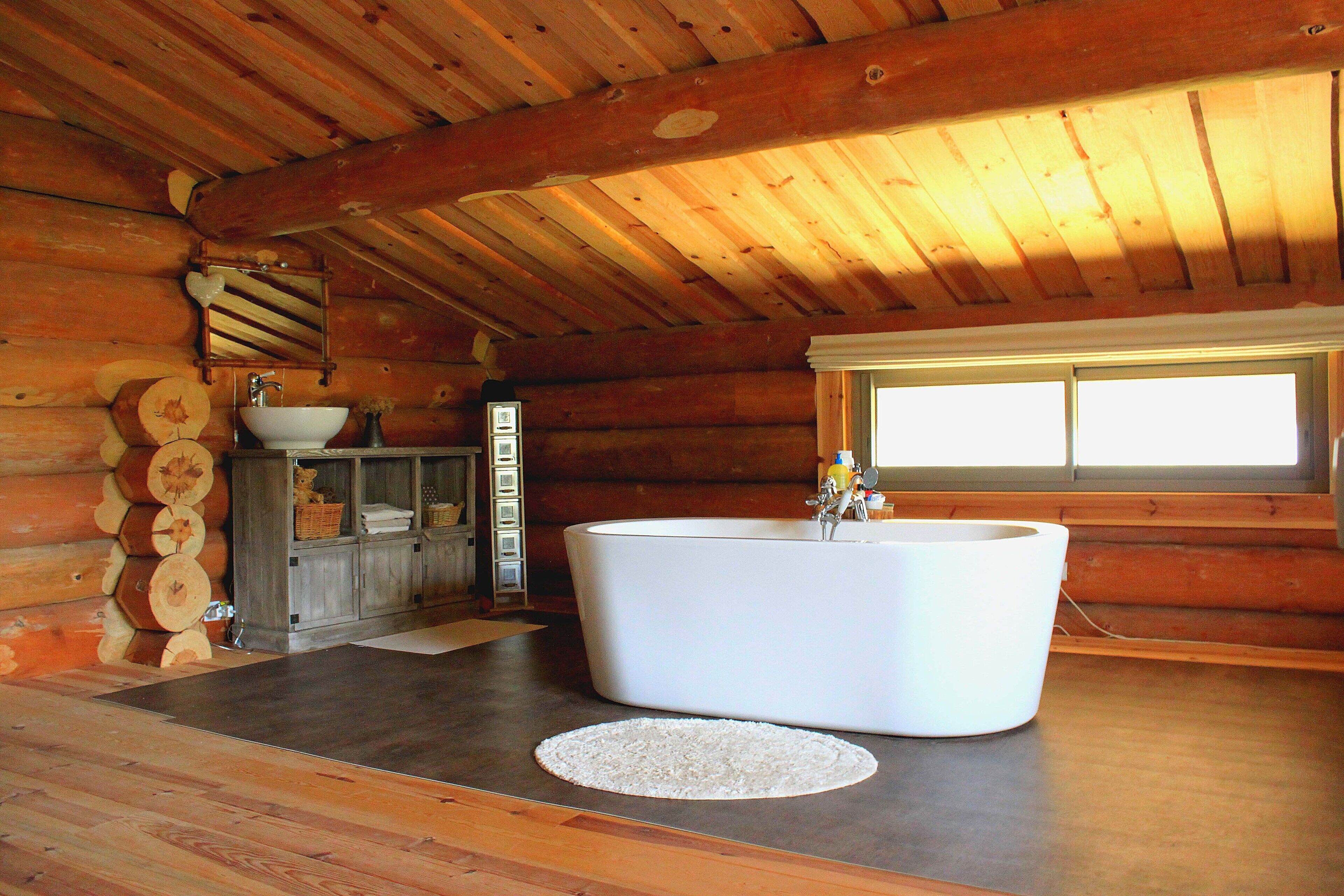 A log cabin bathroom with a large bathtub, wooden walls, and a window providing natural light.