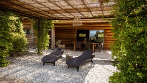 Een overdekt terras met twee lounge fauteuils, een bijzettafeltje en een pergola.