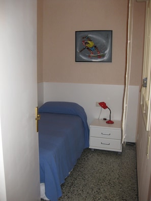 A bedroom with a bed, a nightstand, a red lamp, and a painting on the wall.