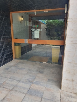 L’entrée d’un hôtel, avec une porte en verre, une enseigne indiquant « ROSAMAR » et un sol carrelé.