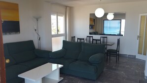 Una sala de estar con un sofá verde, una mesa de centro blanca y un comedor con sillas y una mesa.