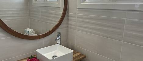 A bathroom with a white sink, wooden vanity, a mirror, and a toilet.
