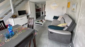 A modern living room with a grey sofa, a dining table with a patterned tablecloth, and a staircase leading to an upper level. - House near castle and beach, sleeps 4, fully equipped (Pornic)