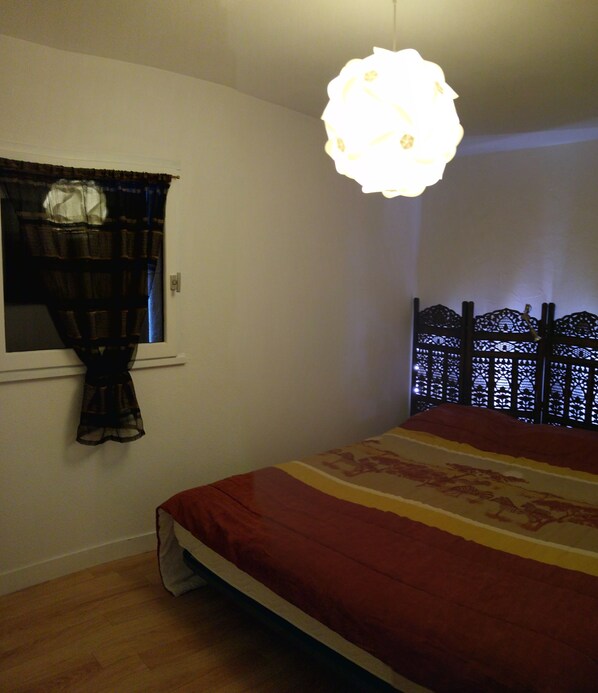 Une chambre à coucher avec un lit, une fenêtre avec des rideaux, un luminaire suspendu et un paravent décoratif.