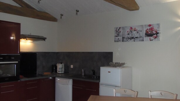 A kitchen with wooden beams, a refrigerator, a dishwasher, and a dining table with chairs.