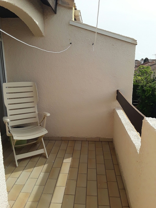A small balcony with a white chair, tiled floor, and a white wall.