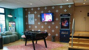 A lobby with a foosball table, seating area, and a TV screen displaying a movie. - 2 steps from Disneyland your apartment for 5! (Serris)