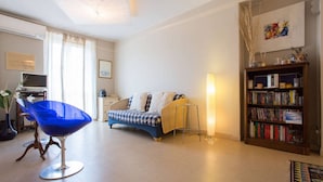 Una sala de estar con una silla azul, un sofá, una estantería y un televisor.