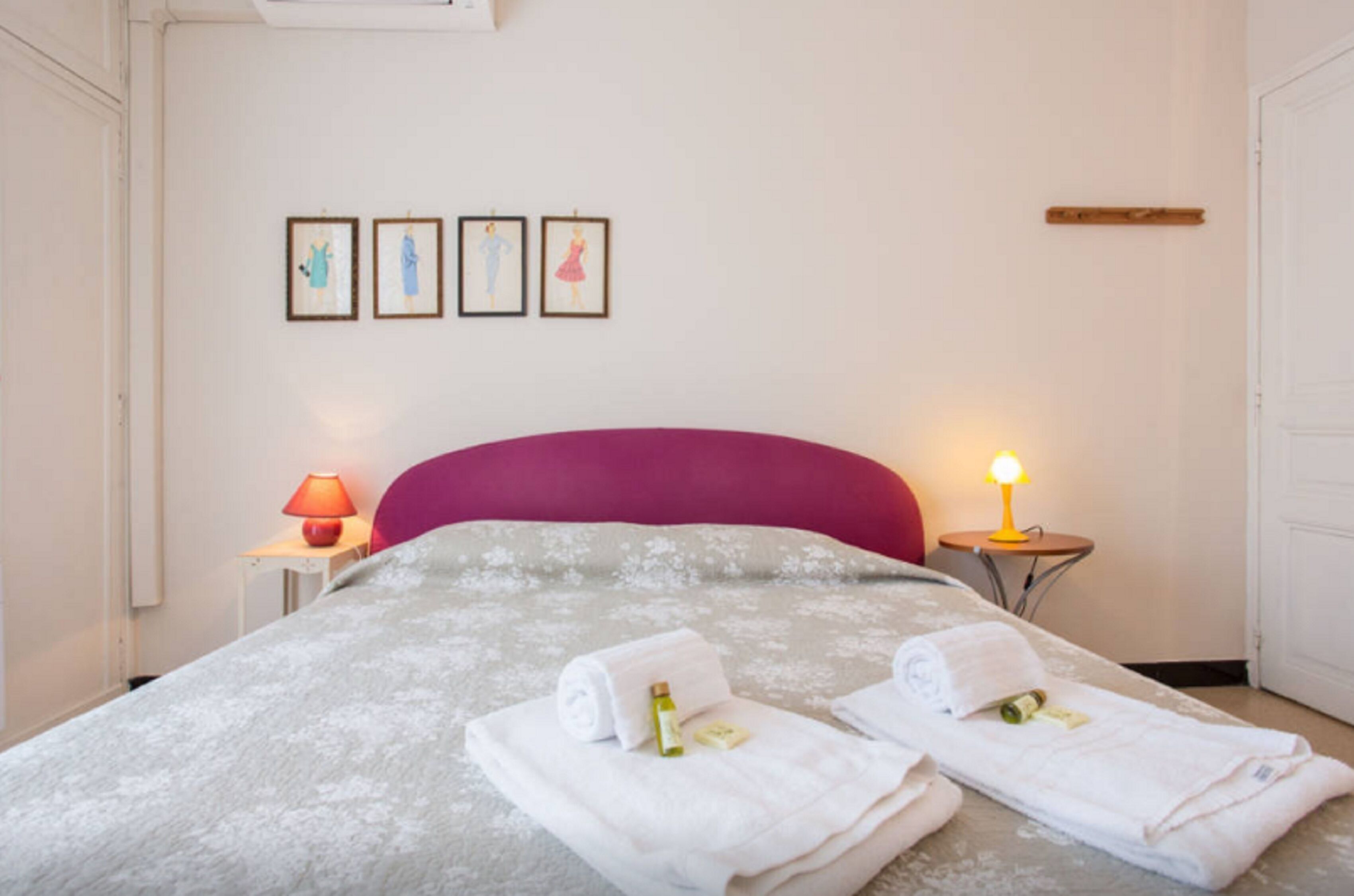 Habitació d'hotel amb un llit, dues taules de nit, una làmpada i obra d'art a la paret.