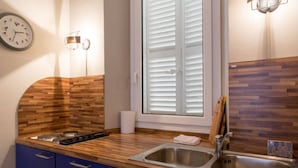 Una cocina con mostrador de madera, estufa, pileta y ventana con persianas.
