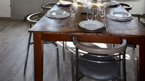 Un comedor con una mesa de madera dispuesta para seis personas, dos ventanas con cortinas a rayas y un mural de peces en la pared.