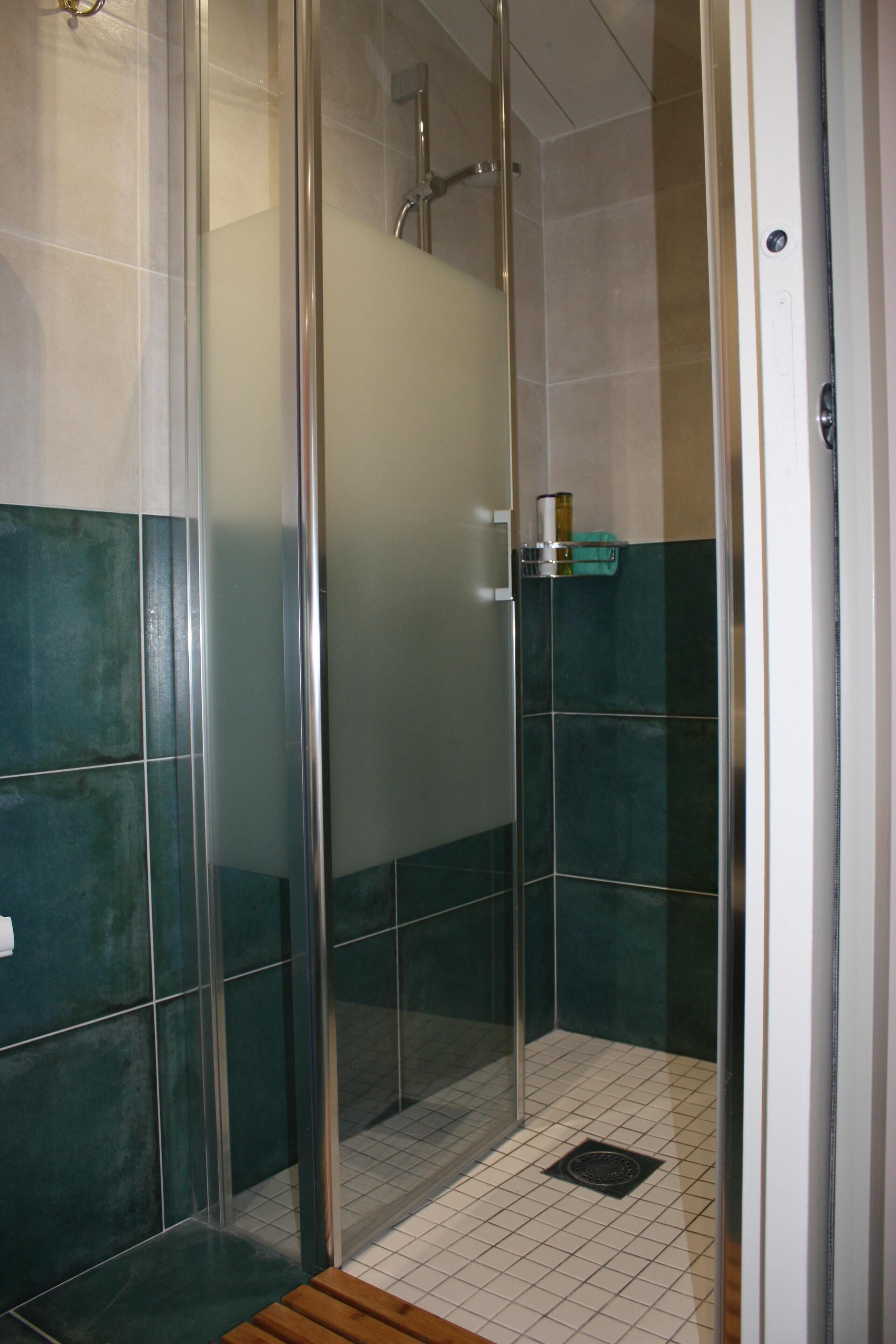 Cabina de dutxa amb vidre, sòl de rajola i una cadira de fusta.