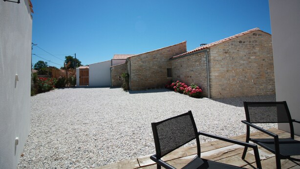 Un patio con suelo de grava, dos edificios de ladrillo y un banco de madera.