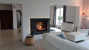 Ein modernes Wohnzimmer mit Kamin, weißen Sofas und einem großen Fenster mit Vorhängen.