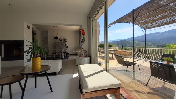 Ein modernes Wohnzimmer mit einem großen Glasfenster, das auf einen Balkon mit Bergblick führt.