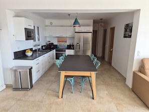A modern kitchen with white cabinets, a black countertop, and a dining area with a wooden table and teal chairs.