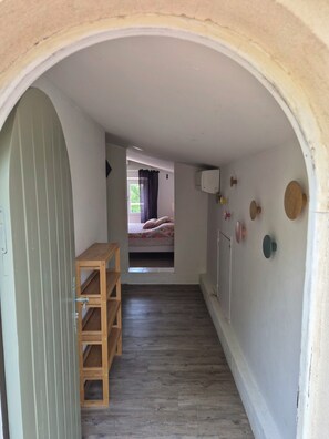 A narrow hallway with a wooden bench, a bed with a floral bedspread, and a wall with various wall-mounted items.