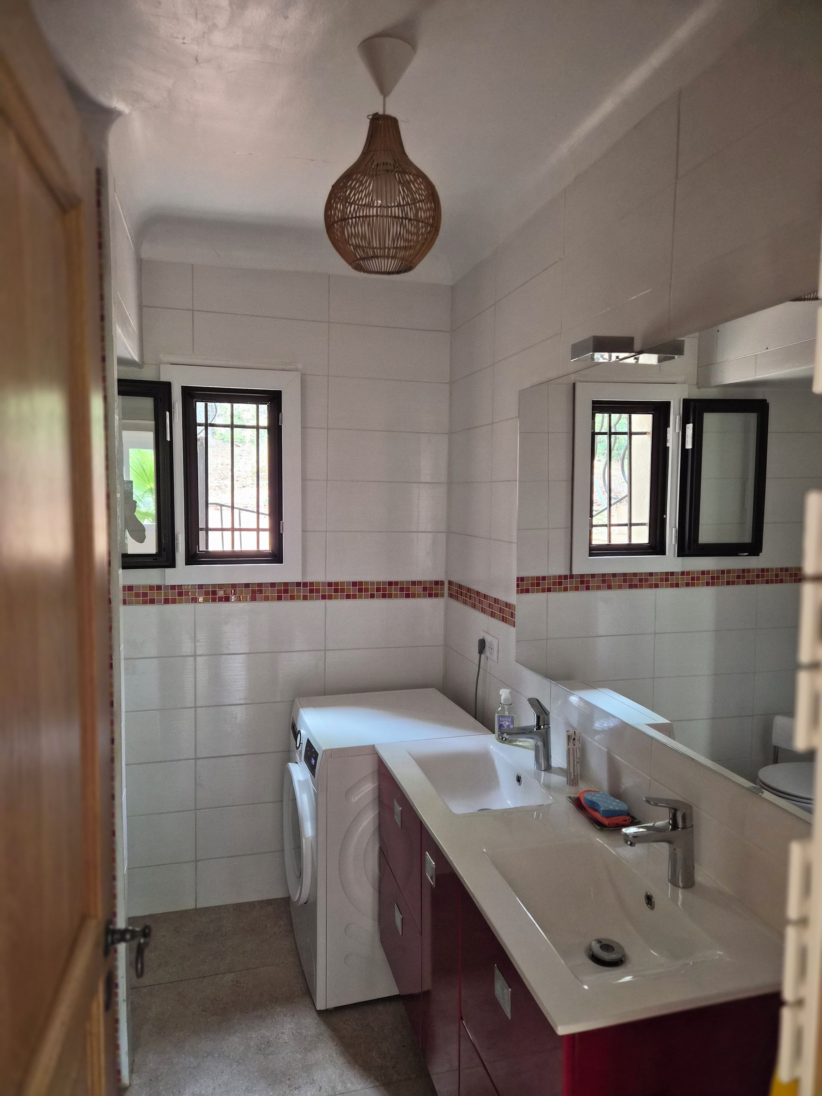 Une petite salle de bain équipée d’un lave-linge, d’un évier, d’un miroir et d’un luminaire suspendu.