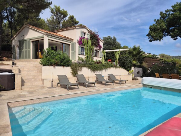 Ein Pool mit Liegestühlen, ein Haus mit Ziegeldach und umliegendes Grün.
