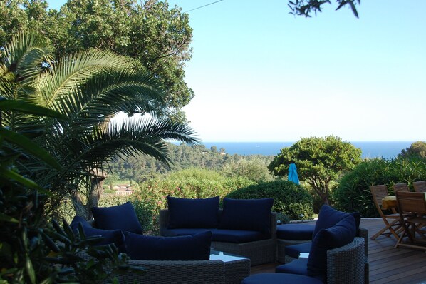 A wicker sofa with cushions, a wooden deck, and a view of the ocean.