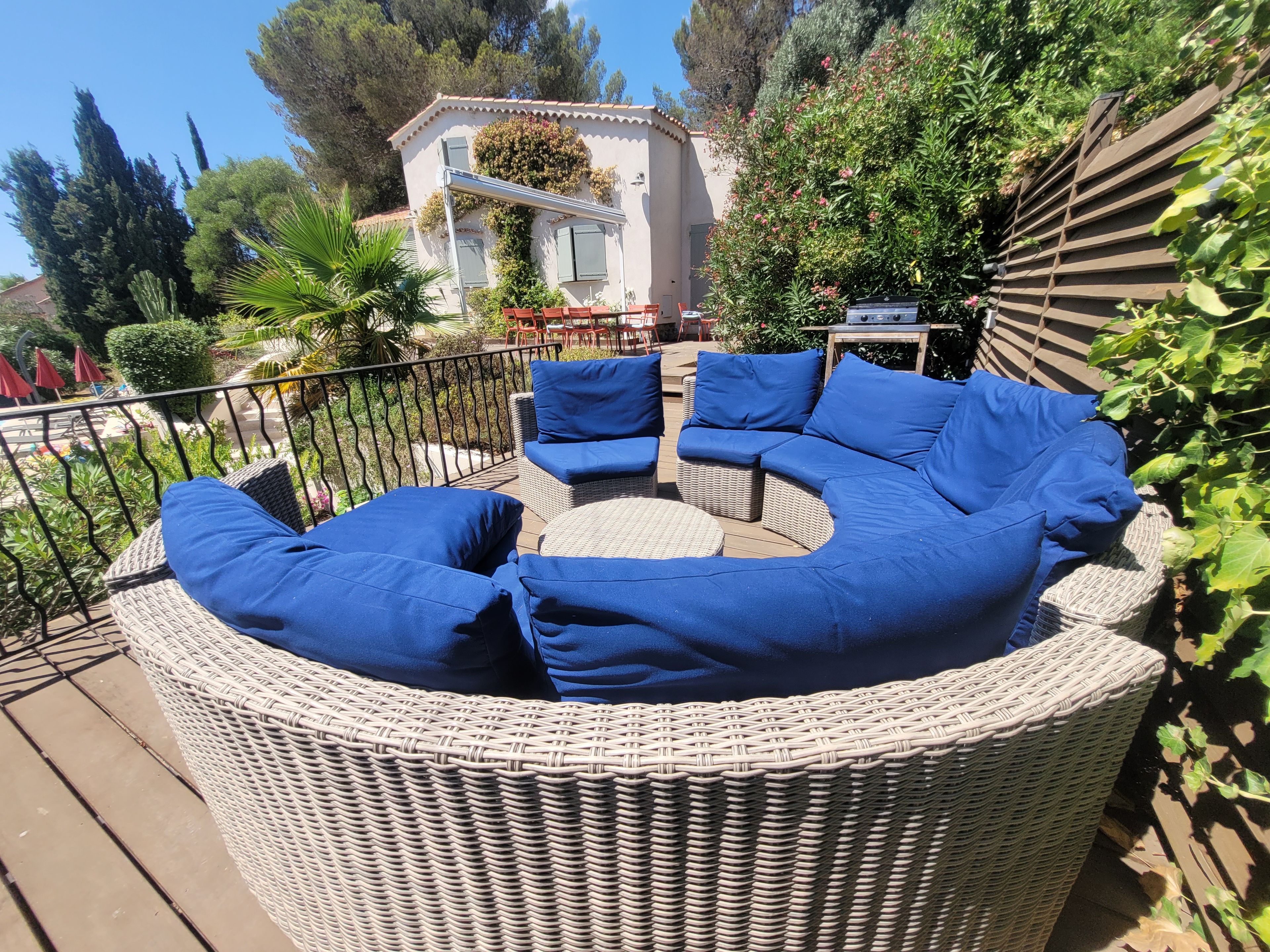A wicker outdoor seating area with blue cushions, a wooden table, and a house with a balcony in the background.