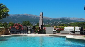 A pool with lounge chairs and a table, surrounded by flowers and a view of mountains. - Provencal bastide with heated pool and air conditioning in Plascassier (Mouans-Sartoux)