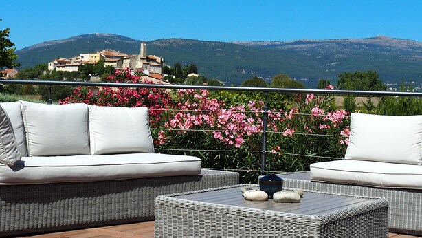 A balcony with wicker furniture and a view of a mountainous town. - Provencal bastide with heated pool and air conditioning in Plascassier (Mouans-Sartoux)