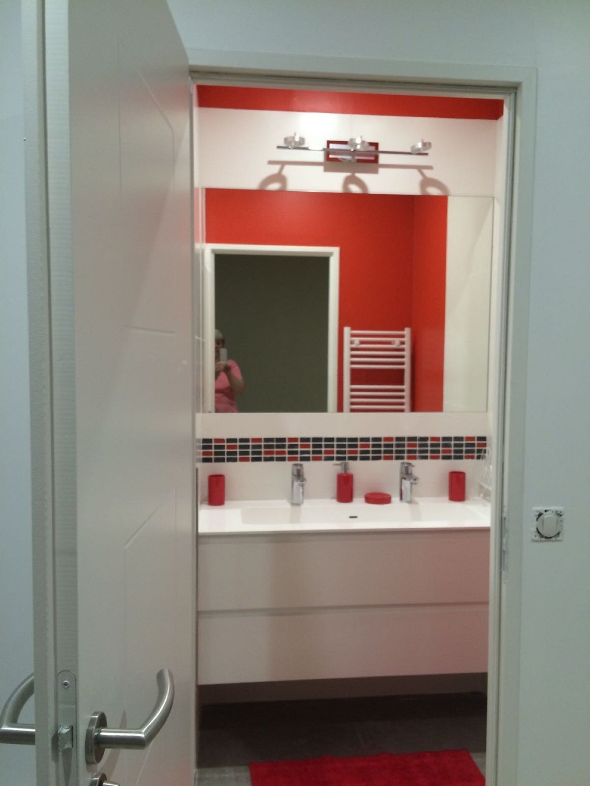 A bathroom with a white sink, red-tiled backsplash, and a mirror above the sink.