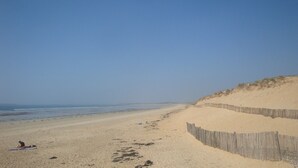 Une plage de sable avec des empreintes, une clôture en bois et un ciel dégagé.