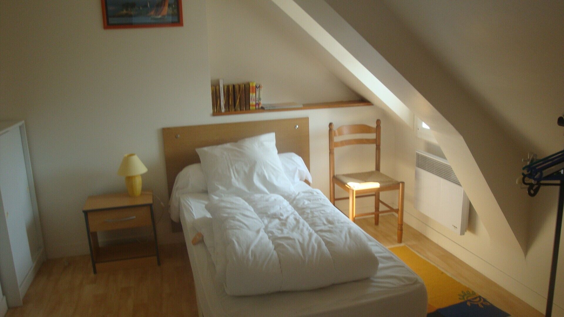 Une chambre à coucher avec un lit, une table de chevet, une chaise et une étagère remplie de livres.