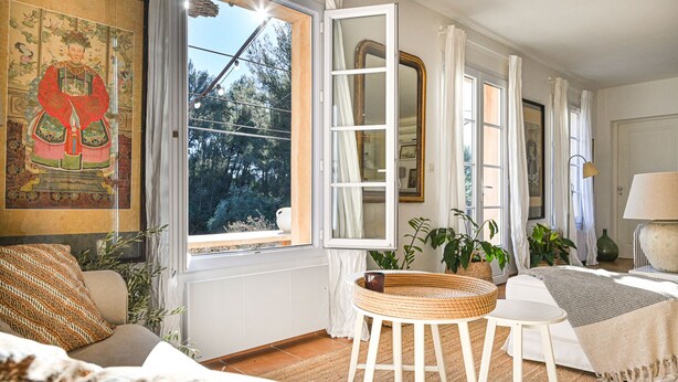 Una habitación con un ventanal grande, un cuadro tradicional, una cama, una silla, una mesa y una lámpara.