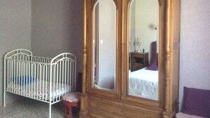 Quarto com guarda-roupa de madeira, berço de metal branco e cadeira roxa.